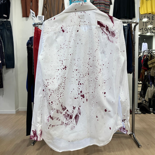 White shirt with red bloodstains on a rack in a store setting