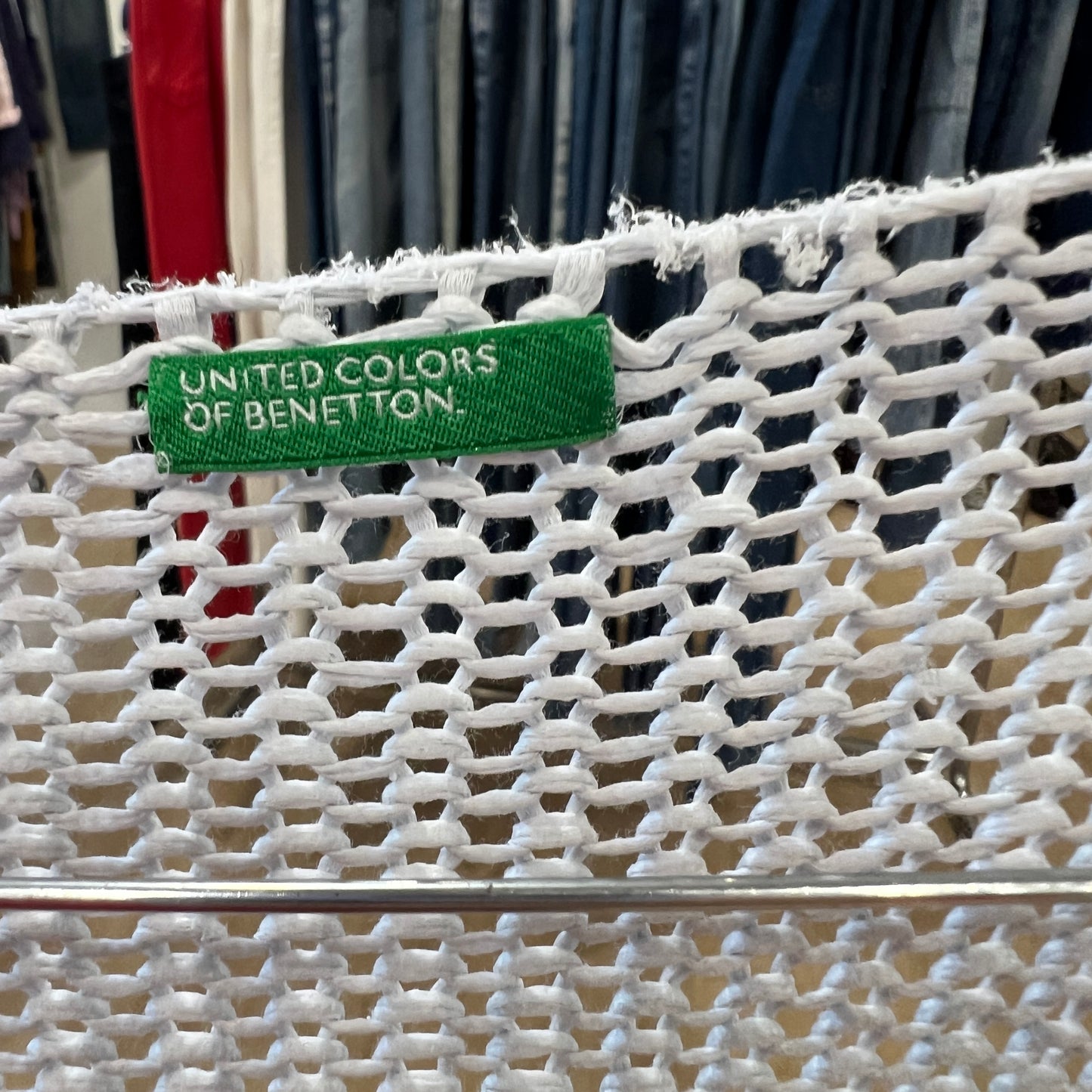 White mesh bag with a green 'United Colors of Benetton' label against a clothing background