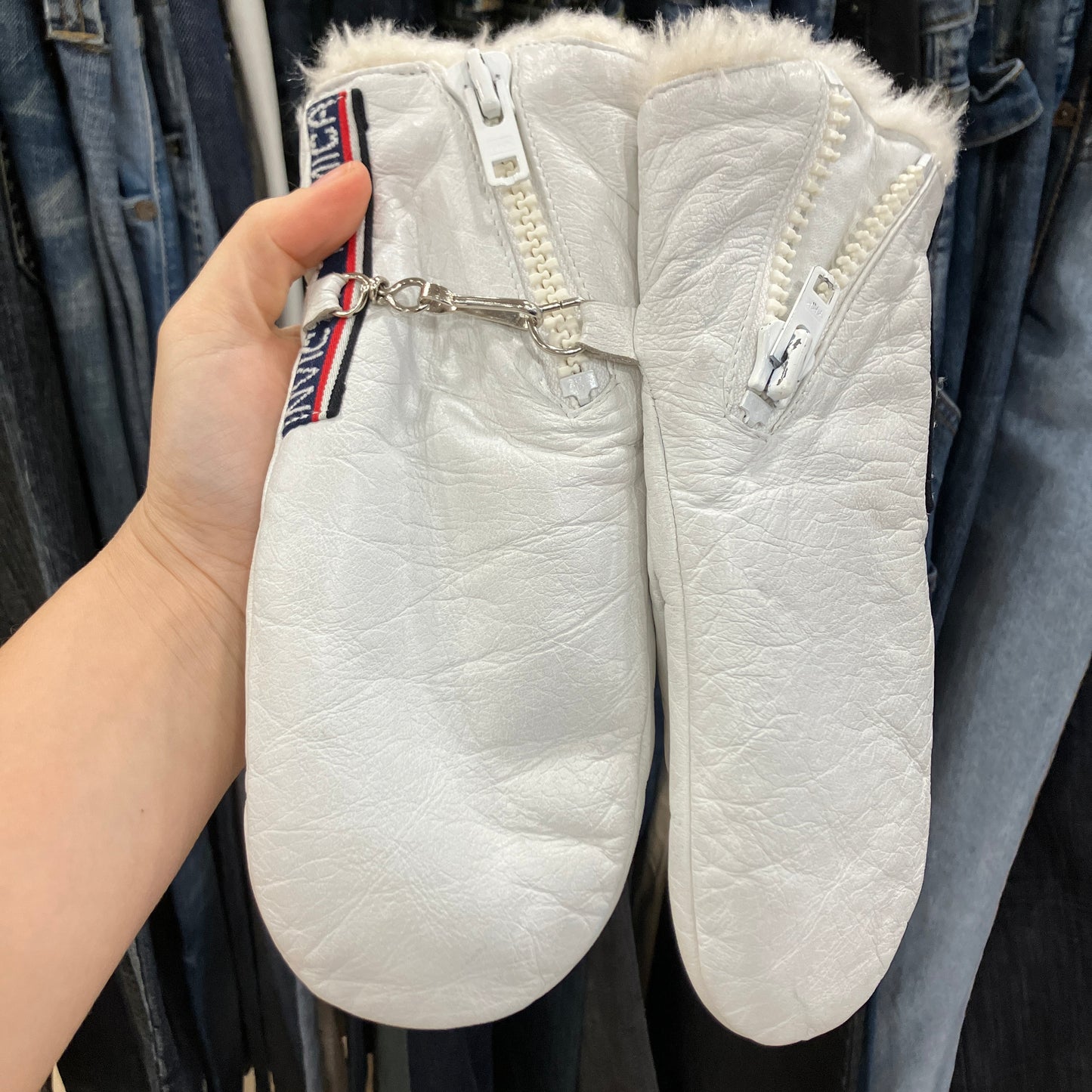 White mittens with fur lining held by a hand against a clothing background