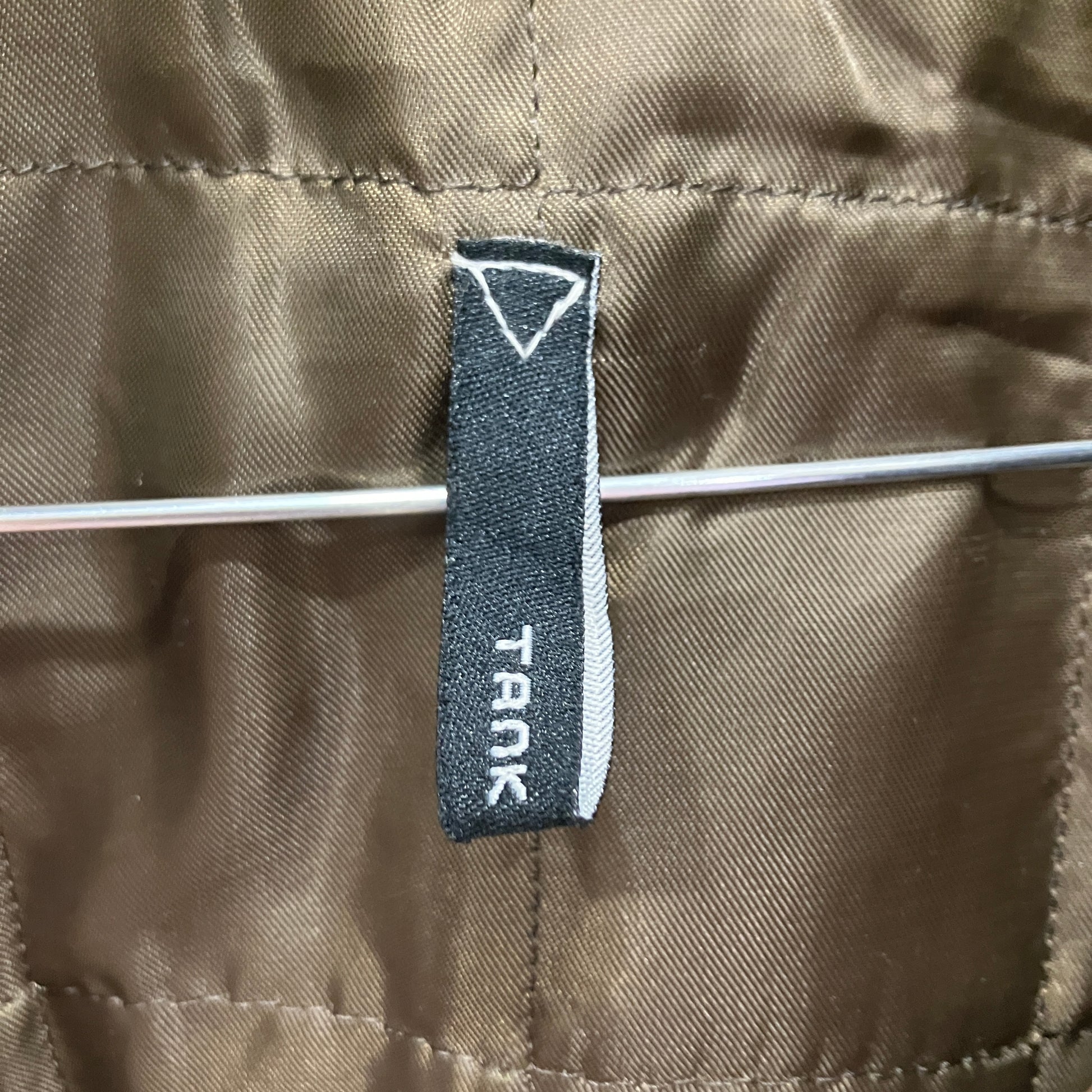 Close-up of a 'Tank' tag on a brown fabric surface