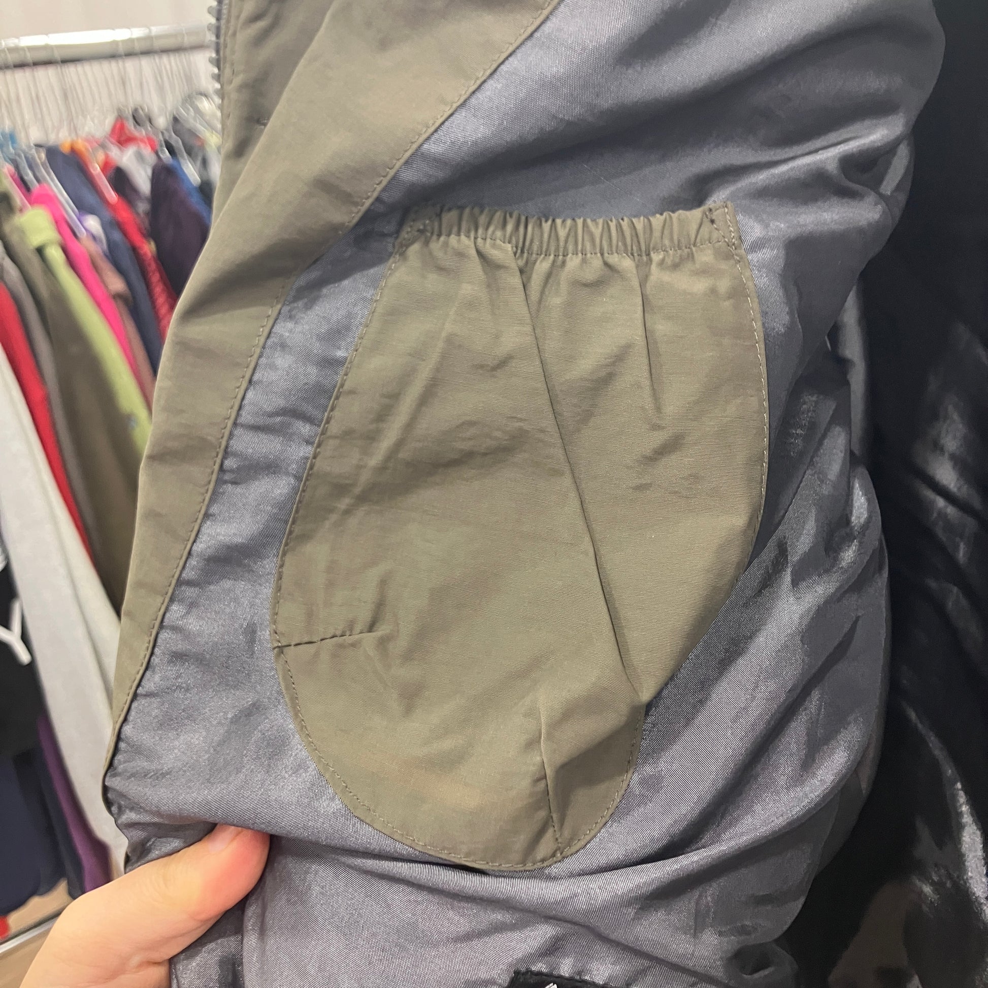 Gray jacket with a green patch held by a hand against a clothing store background