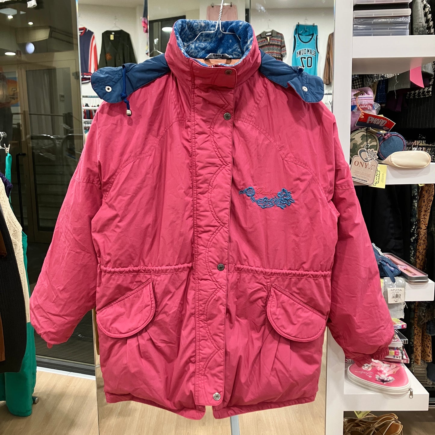 Pink children's coat with blue lining on a hanger in a store setting