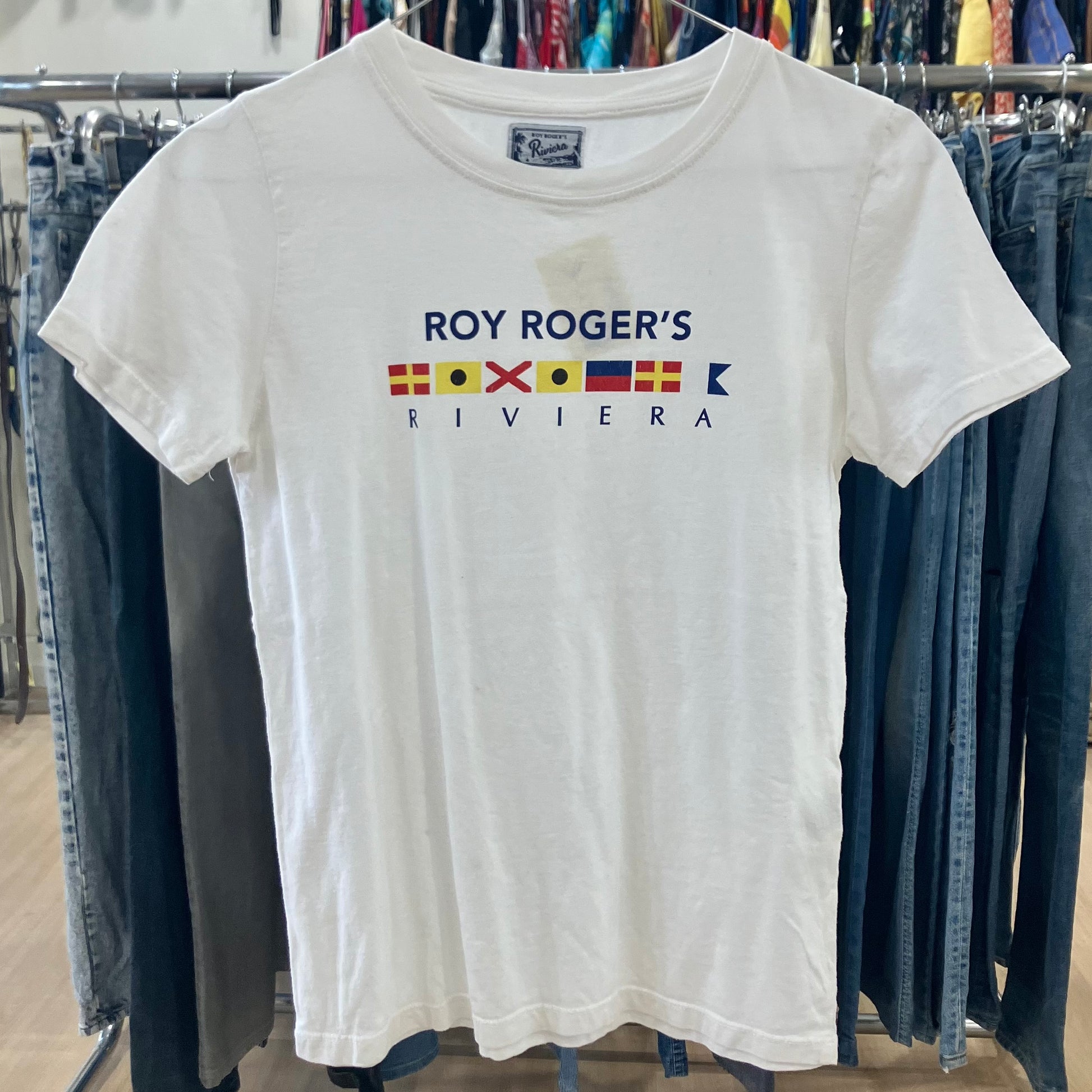 White t-shirt with 'Roy Roger's Riviera' logo on a rack with jeans