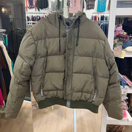 Green puffer jacket hanging in a store with clothing racks in the background