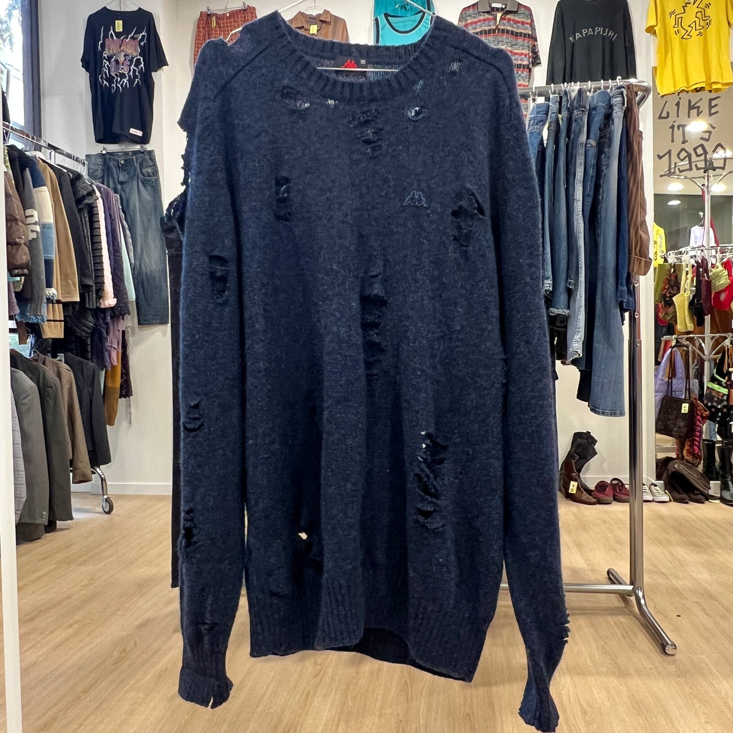 Blue distressed sweater in a clothing store with racks of clothes in the background