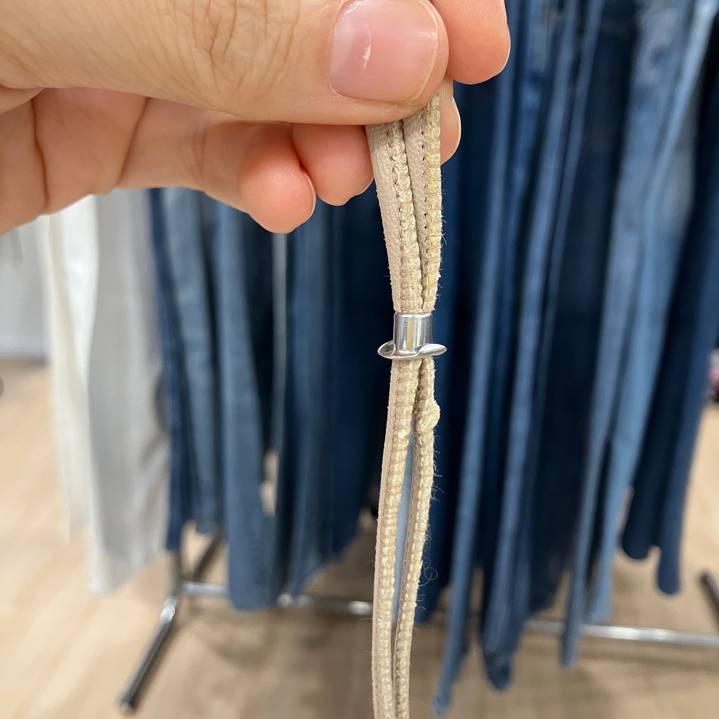 Close-up of a hand holding beige shoelace with metal eyelet against a blurred background