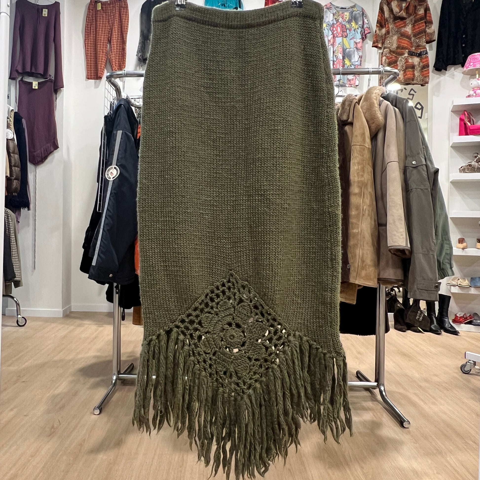 Green knitted skirt with fringe and crochet detail in a clothing store setting