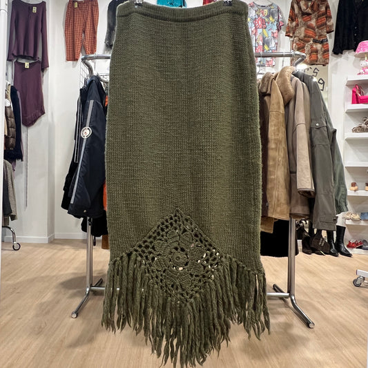 Green knitted skirt with fringe and crochet detail in a clothing store setting