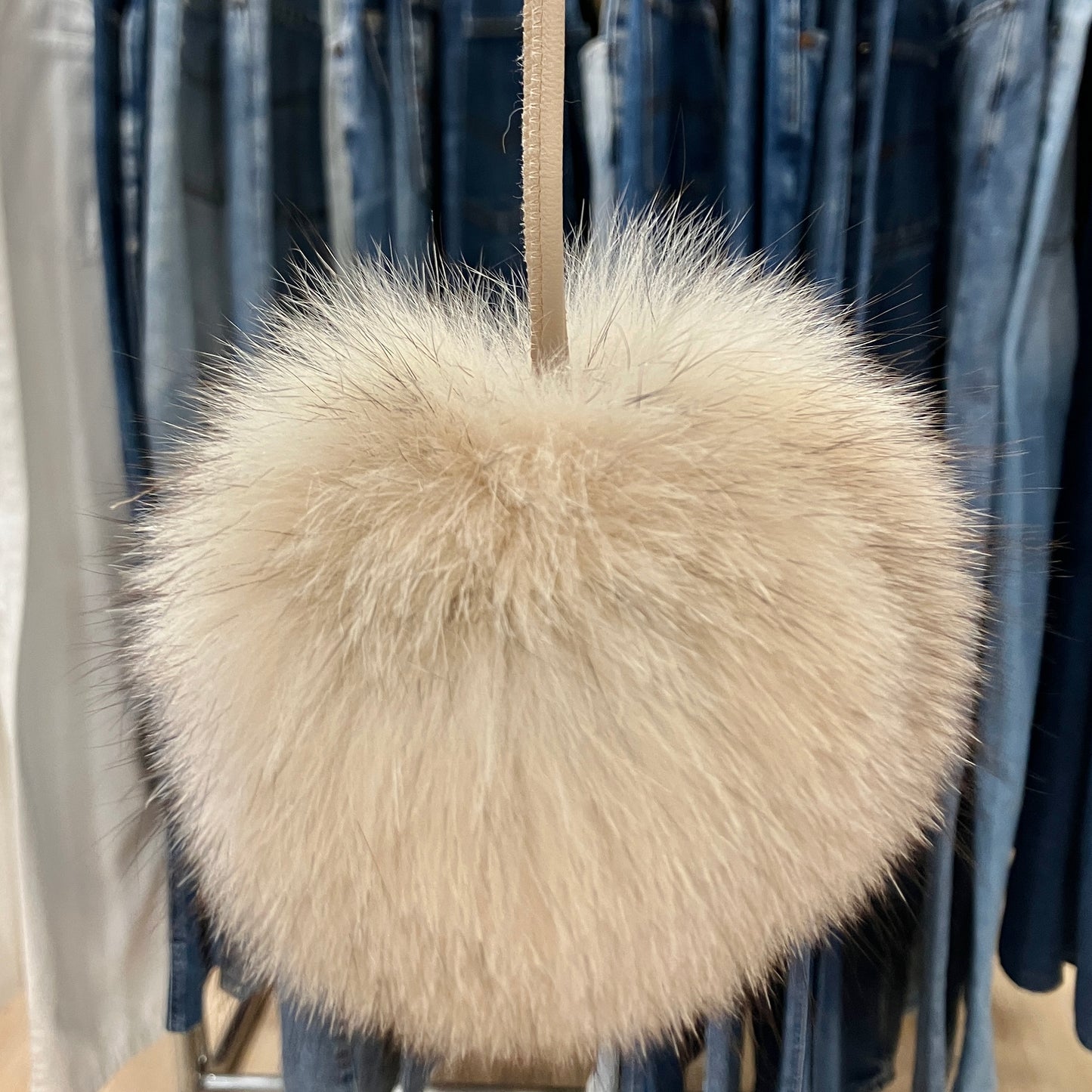 Beige fluffy bag hanging on a rack with jeans in the background