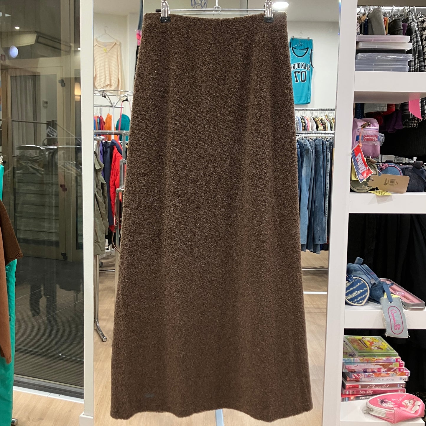 Brown skirt hanging in a store with shelves and clothing in the background