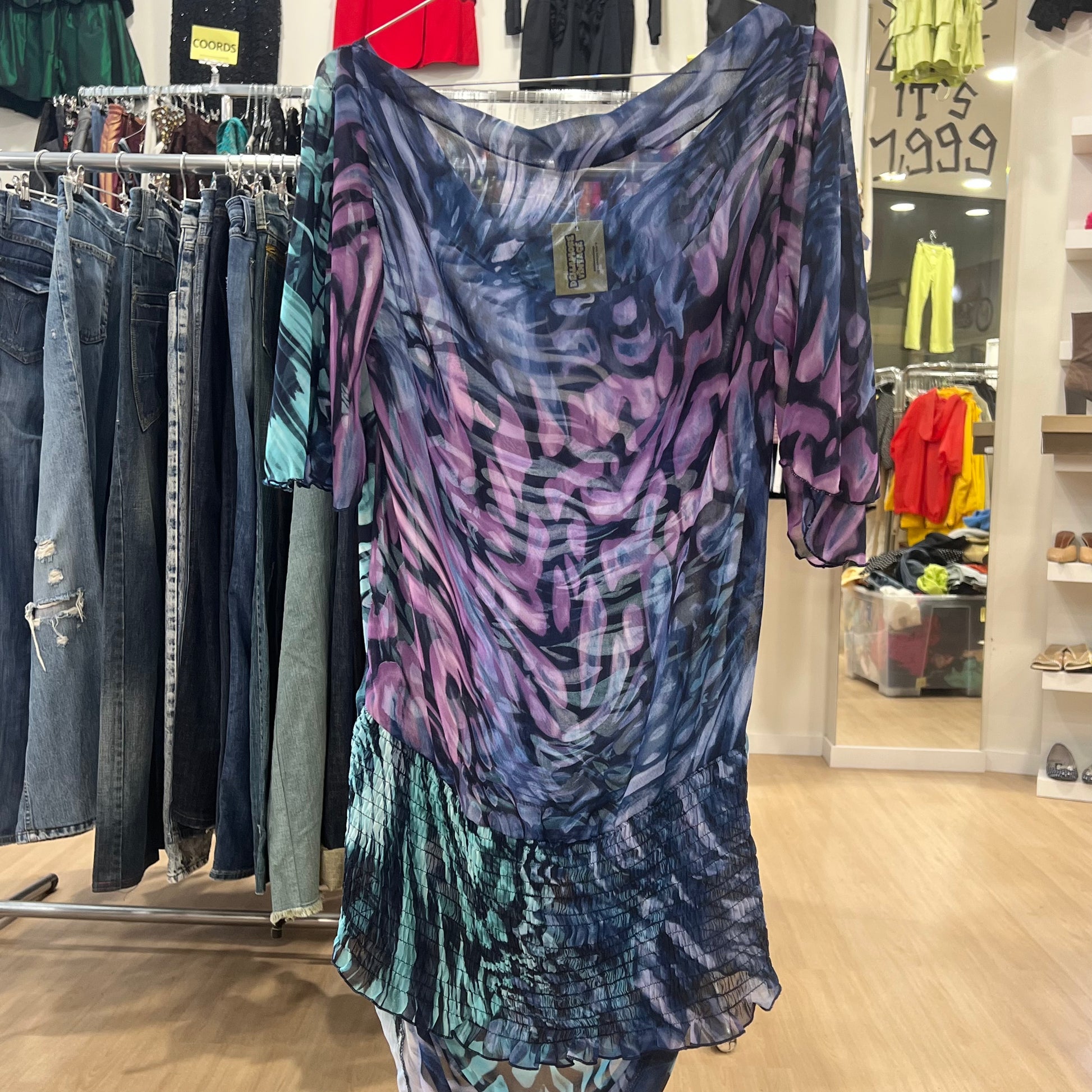 Colorful patterned dress hanging in a store with clothing racks and displays in the background