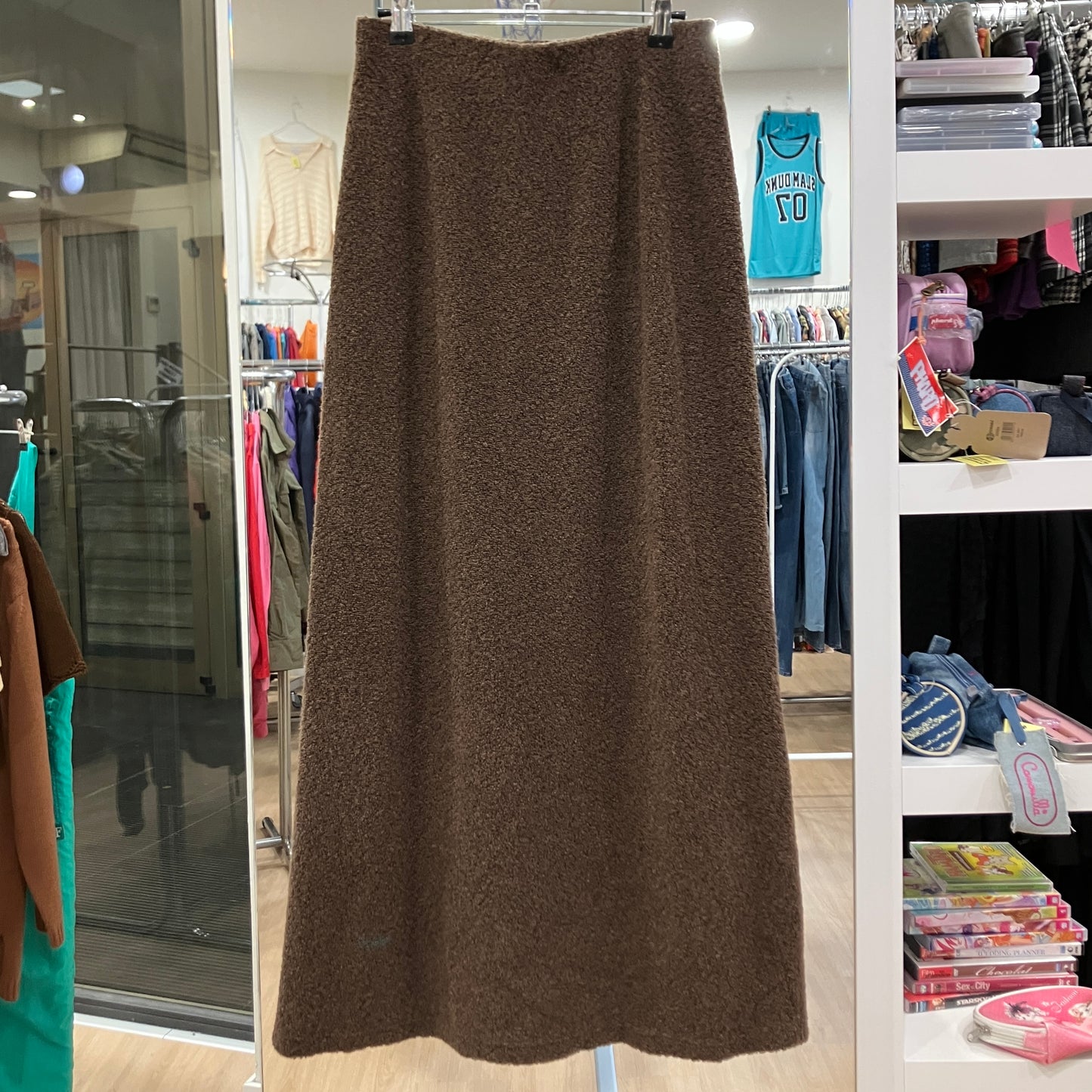 Brown skirt hanging in a store with clothing racks and shelves in the background