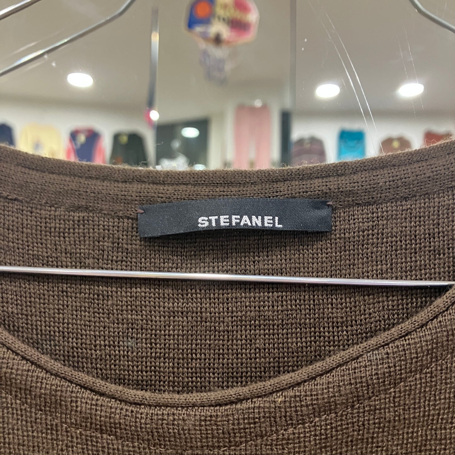 Brown fabric with a 'STEFANEL' label on a hanger in a store setting