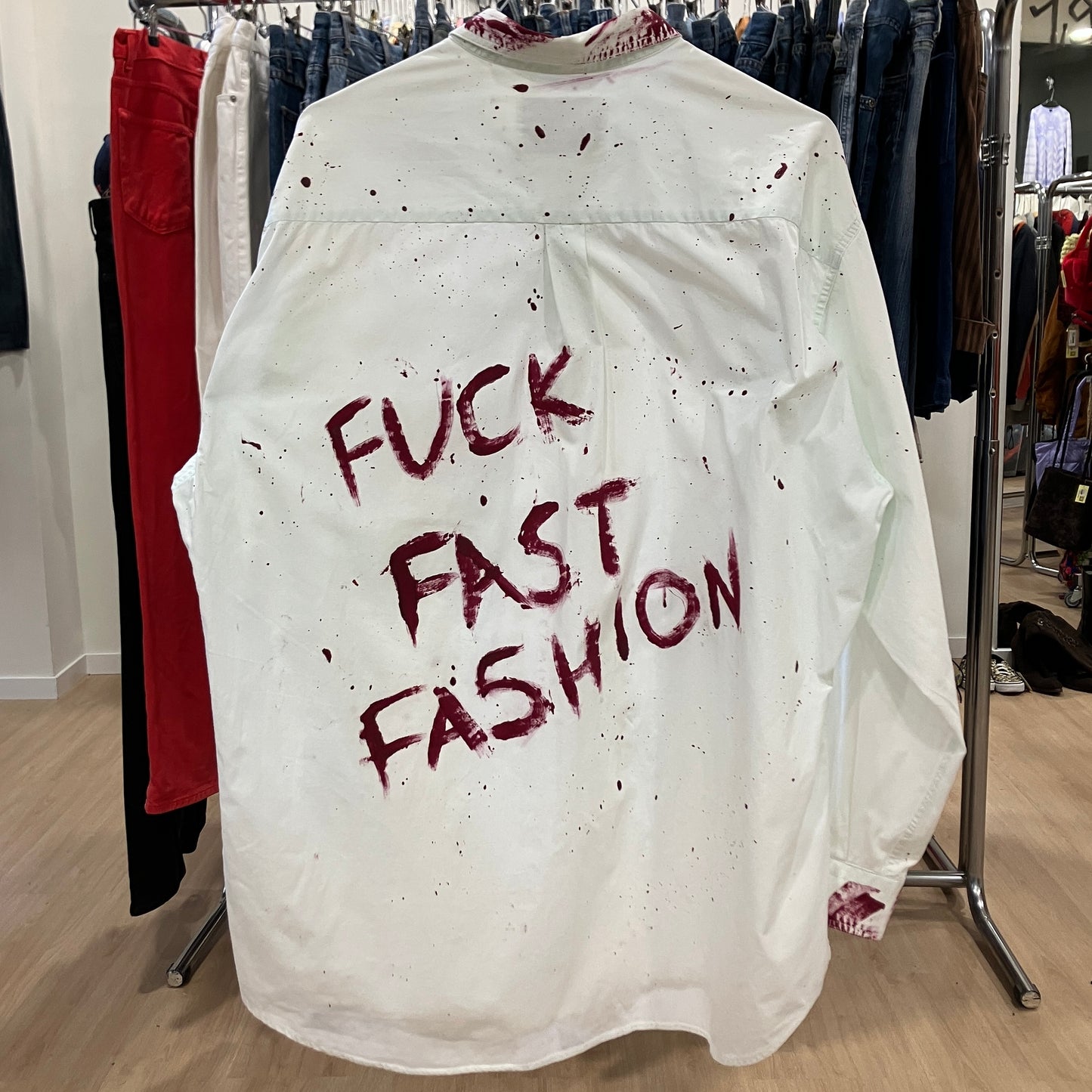 White shirt with red text 'FUCK FAST FASHION' on a rack in a clothing store