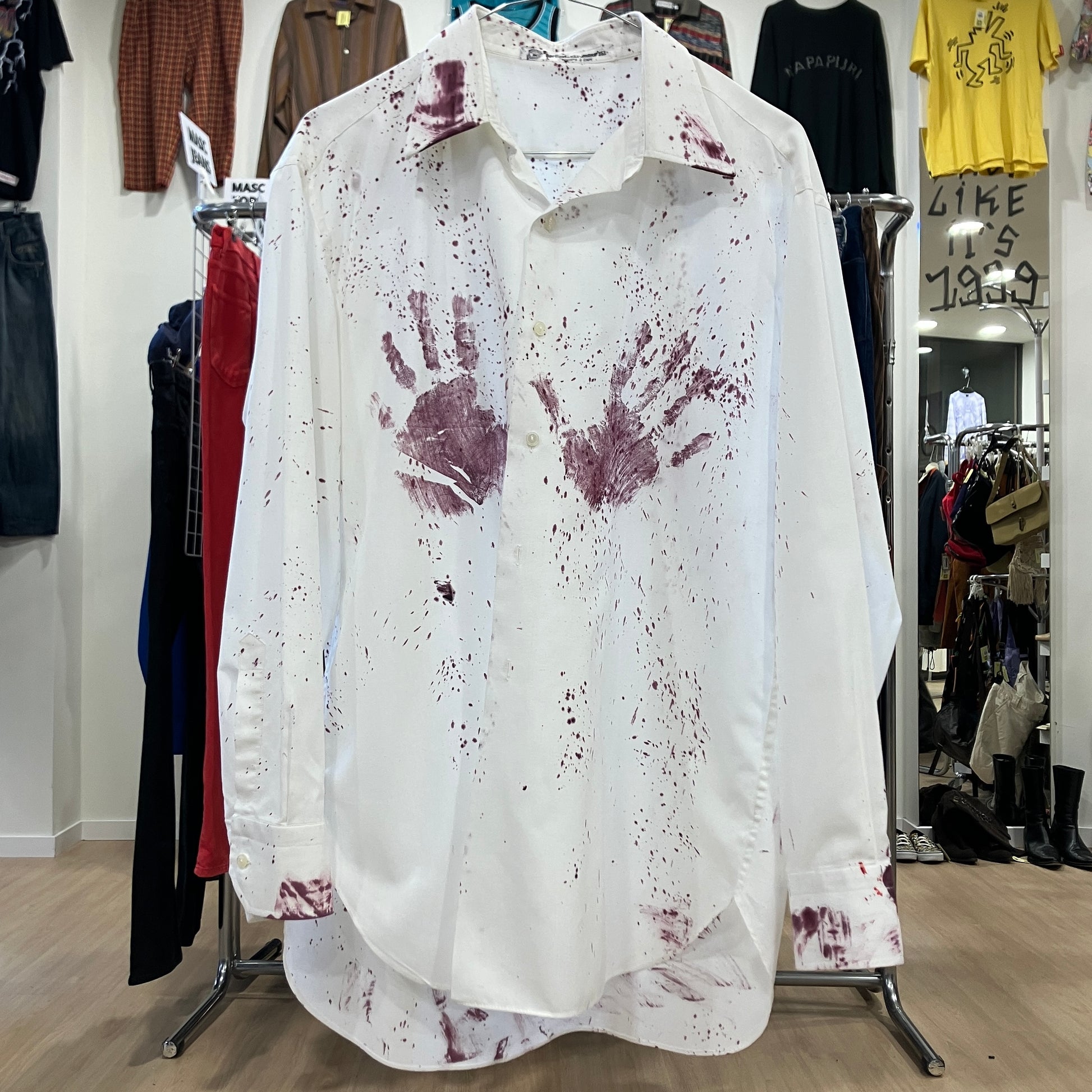 White shirt with red handprints on a rack in a store setting