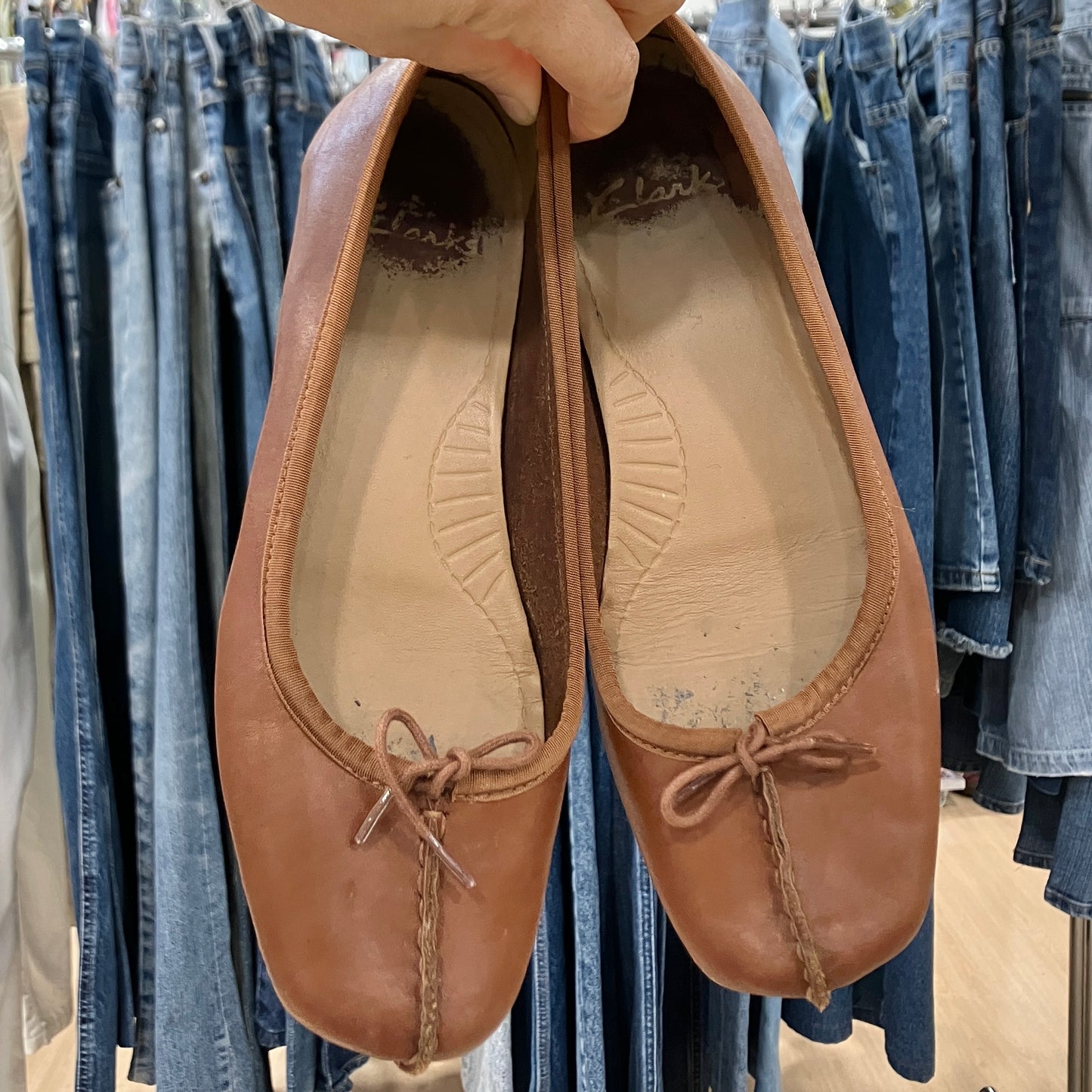 Brown leather shoes held in front of denim clothing racks