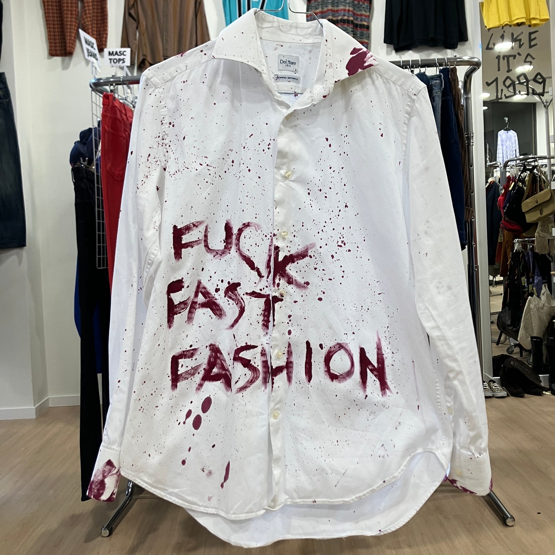 White shirt with red text 'FUCK FAST FASHION' on a clothing rack in a store