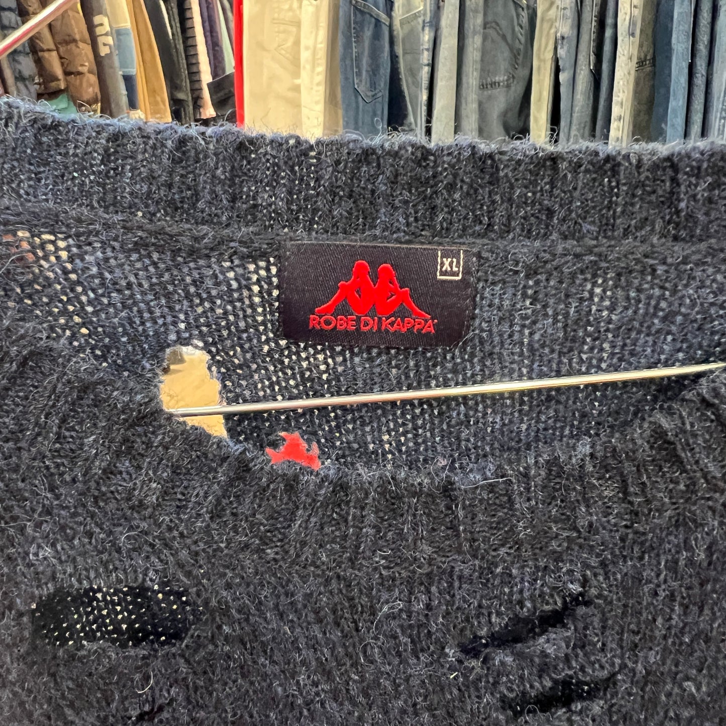 Dark blue sweater with a brand label on a clothing rack background