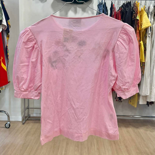 Pink blouse with sheer overlay on a hanger against a clothing store background