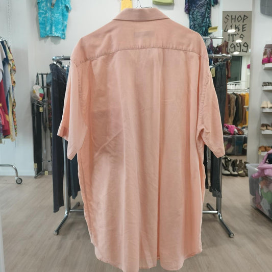 Pink shirt on a hanger in a store setting with racks and clothing in the background