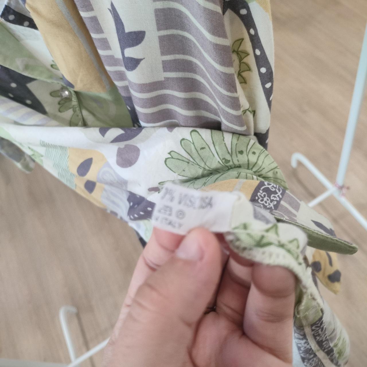 Hand holding a fabric swatch with a pattern of leaves and flowers, showing a brand label
