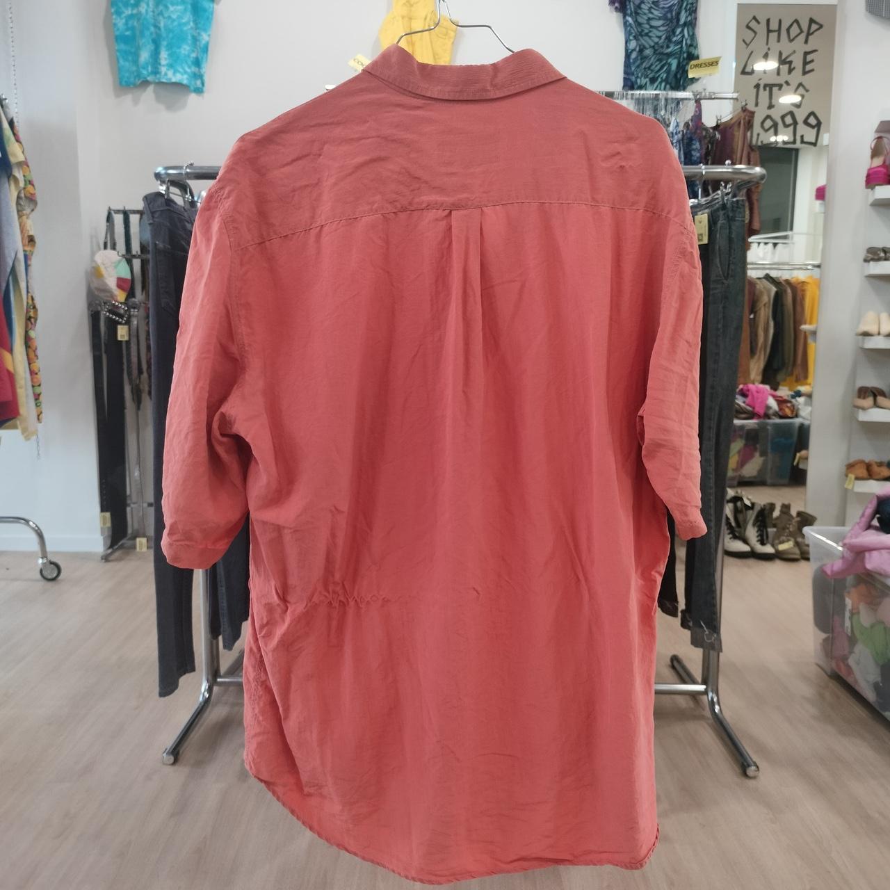 Red shirt on a hanger in a store setting with clothing racks and shelves in the background